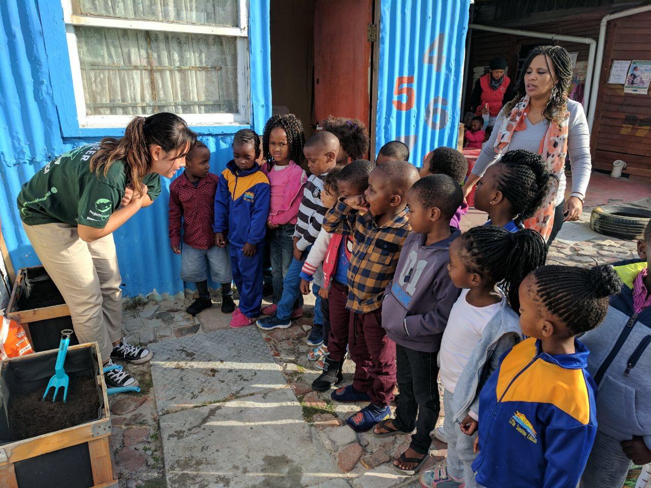 An intern from Projects Abroad is talking to a group of children promoting healthy eating and teaching them how to grow vegetables as part of her nutrition internship in South Africa. A female intern from Projects Abroad is pictured teaching a group of children about growing vegetables as part of her nutrition internship in South Africa.
